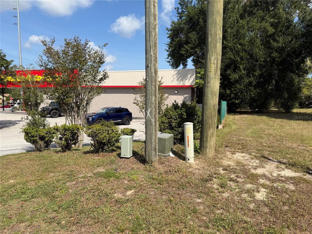 A grassy lot features two utility poles, electrical boxes, and a commercial building in the background — 121 W LEMON STREET, LADY LAKE, FL