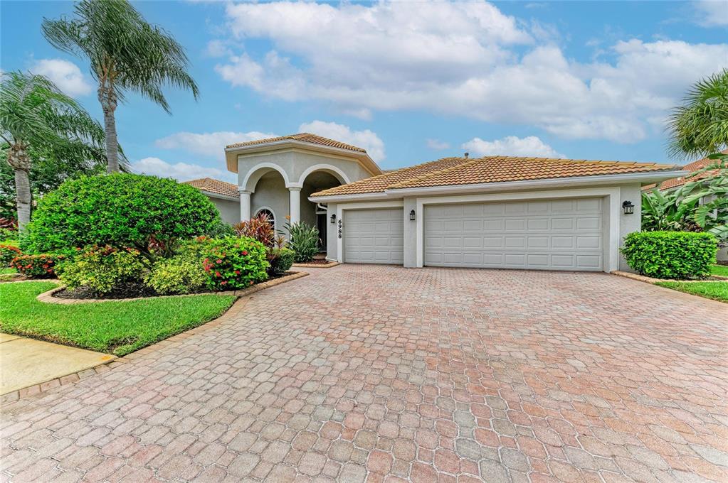 A single-story house with a three-car garage and a paved driveway under a blue sky — 6988 74TH STREET CIRCLE E, BRADENTON, FL