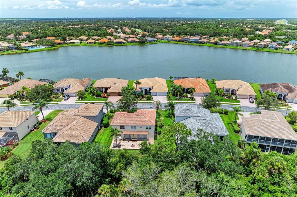 An aerial view shows a row of suburban houses along a lake with lush trees — 6988 74TH STREET CIRCLE E, BRADENTON, FL