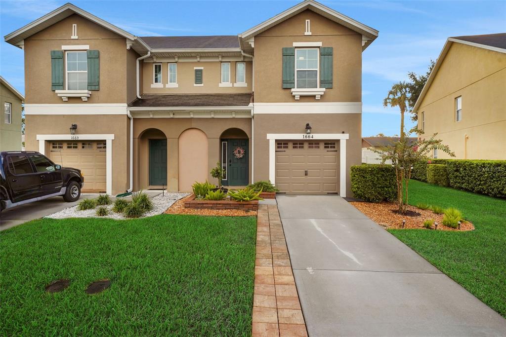 A two-story duplex house features tan stucco siding, green shutters, and two separate garage doors — 1664 PETERSON PLACE, SANFORD, FL