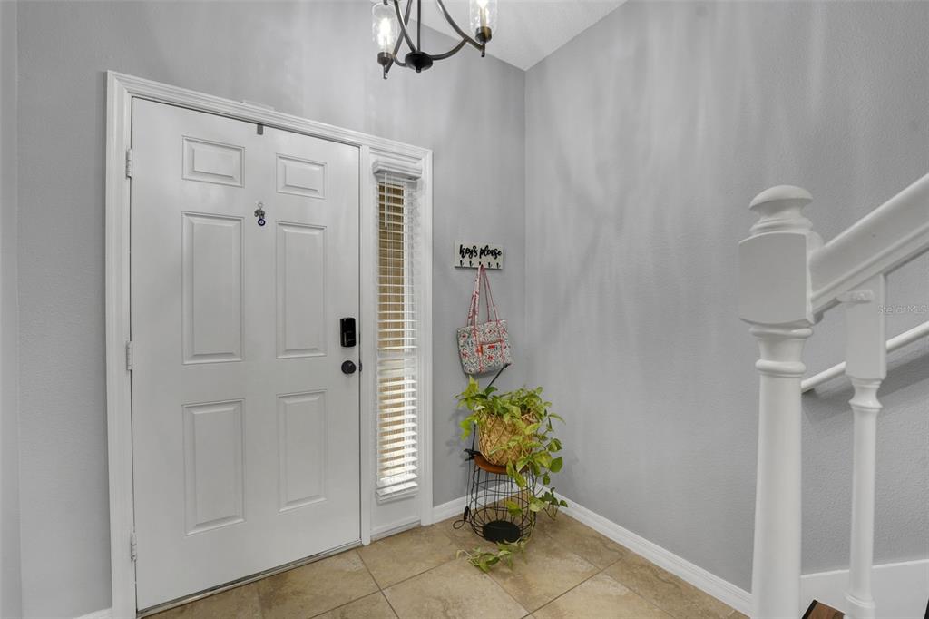 An entryway features a white front door, tiled flooring, a small plant, and a staircase railing — 1664 PETERSON PLACE, SANFORD, FL
