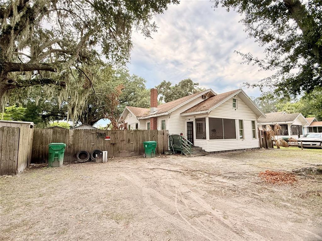 A white house with a screened porch and a brick chimney stands behind a wooden fence — 208 3RD STREET, WINTER GARDEN, FL