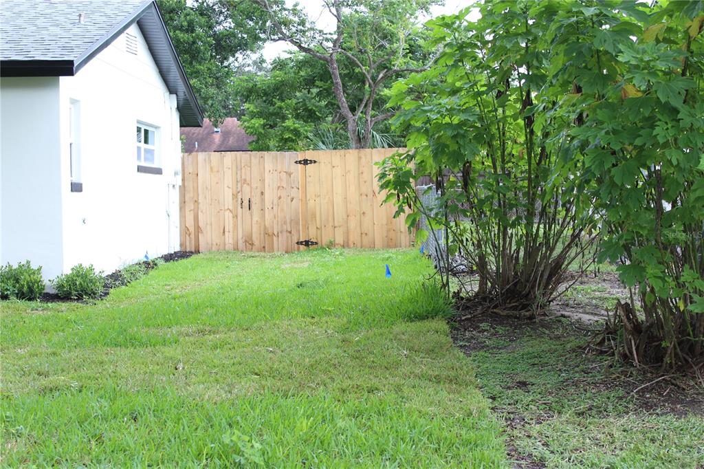 A side view of a white house exterior with a wooden fence and green landscaping — 7015 CRESTLAKE DRIVE, ORLANDO, FL