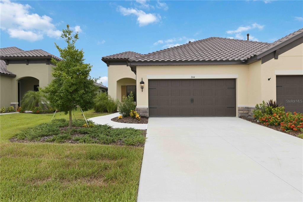 A tan house exterior features a brown garage door, a concrete driveway, and landscaped lawn — 244 ALTAMURA CIRCLE, NOKOMIS, FL