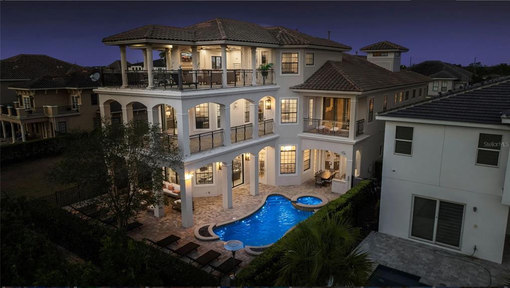 An aerial view of a multi-story house at dusk featuring a pool and covered balconies — 304 MUIRFIELD LOOP, REUNION, FL