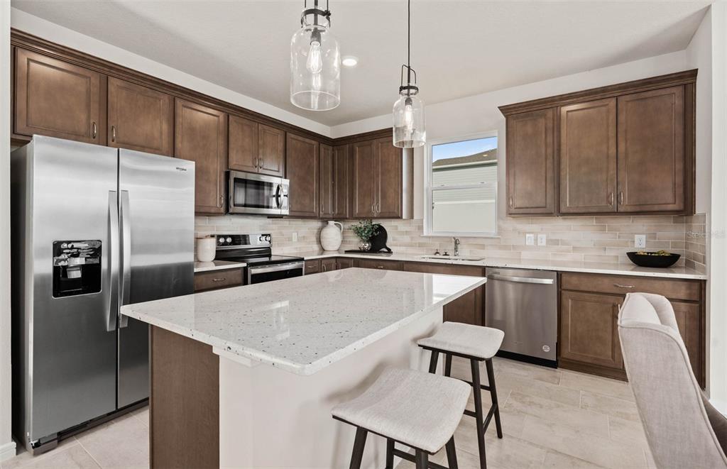 A kitchen features dark wood cabinets, a white speckled island, and stainless steel appliances — 5514 FREESIA DRIVE, LAKELAND, FL