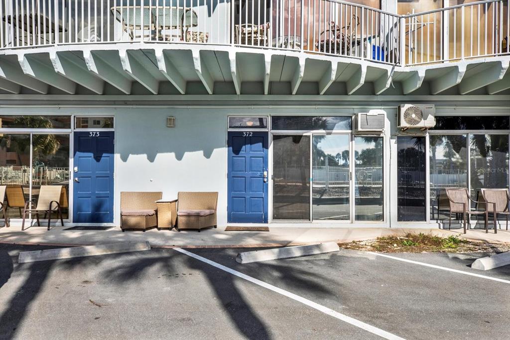 The exterior of a two-story building features blue doors, patio furniture, and parking spaces — 18399 GULF BLVD UNIT 372, INDIAN SHORES, FL