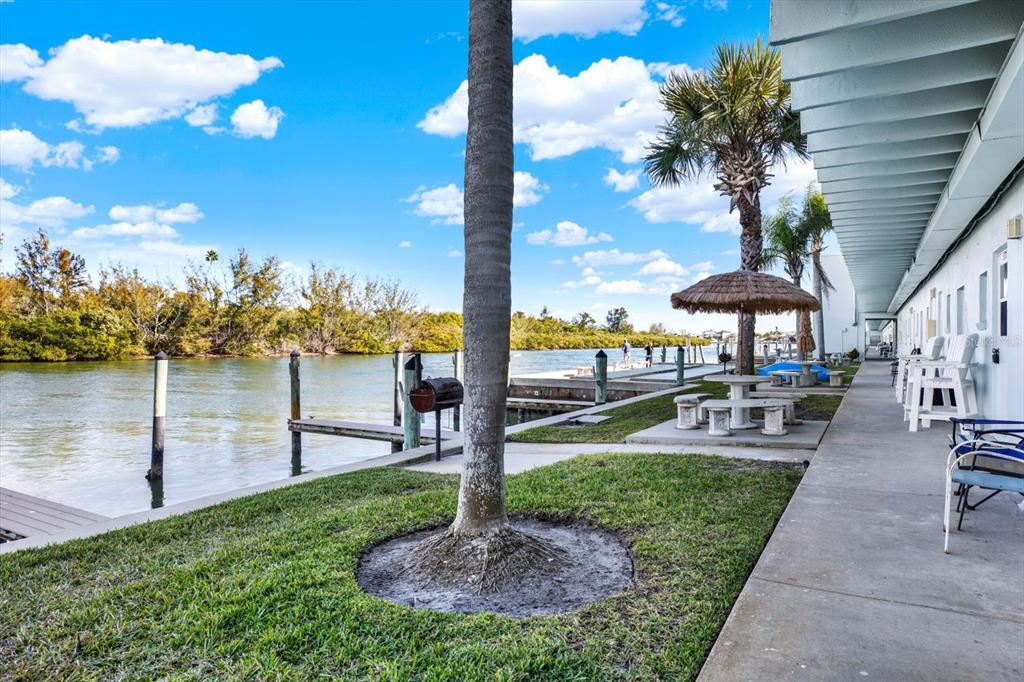 A waterfront patio area features a palm tree, a picnic table, and a boat dock — 18399 GULF BLVD UNIT 372, INDIAN SHORES, FL