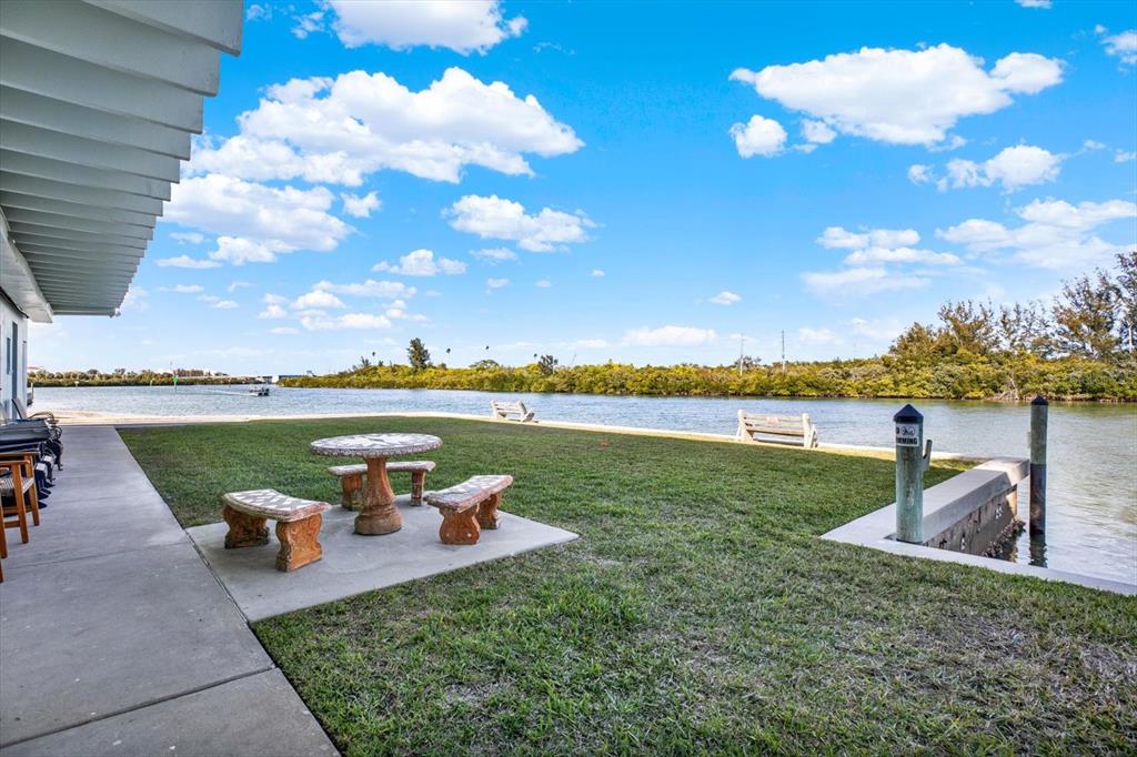 A concrete patio with a stone table and benches overlooks a grassy lawn and canal — 18399 GULF BLVD UNIT 372, INDIAN SHORES, FL