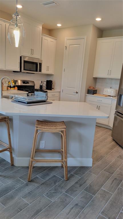 A kitchen features white cabinetry, a quartz island with two stools, and gray wood-look flooring — 5419 SUMMIT GLEN, BRADENTON, FL