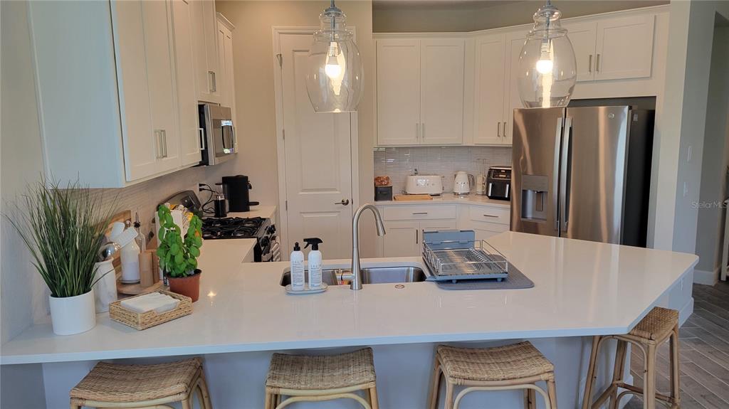 A modern kitchen features white cabinetry, quartz countertops, stainless steel appliances, and a breakfast bar — 5419 SUMMIT GLEN, BRADENTON, FL