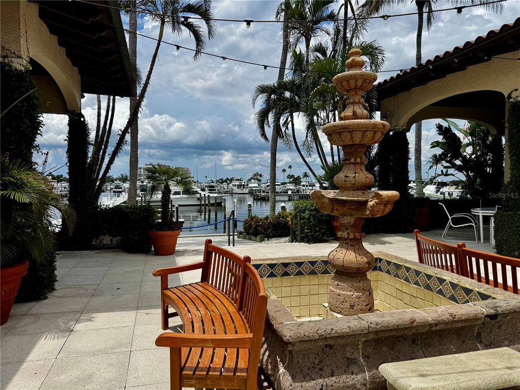 A stone fountain sits on a patio with wooden benches overlooking a boat marina — 2600 HARBOURSIDE DRIVE UNIT C11, LONGBOAT KEY, FL
