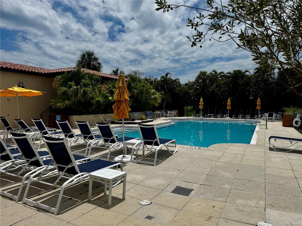 A swimming pool surrounded by lounge chairs, umbrellas, and palm trees under a cloudy sky — 2600 HARBOURSIDE DRIVE UNIT C11, LONGBOAT KEY, FL