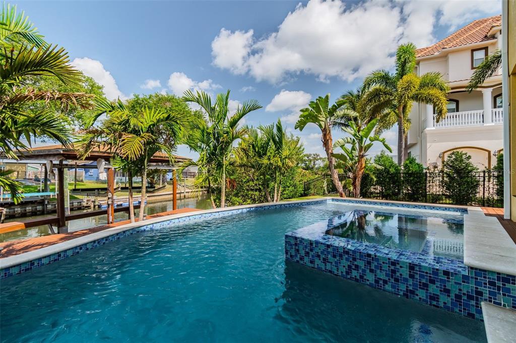 A backyard swimming pool with a tiled spa overlooks a canal lined with palm trees — 539 TREVISO DRIVE, APOLLO BEACH, FL