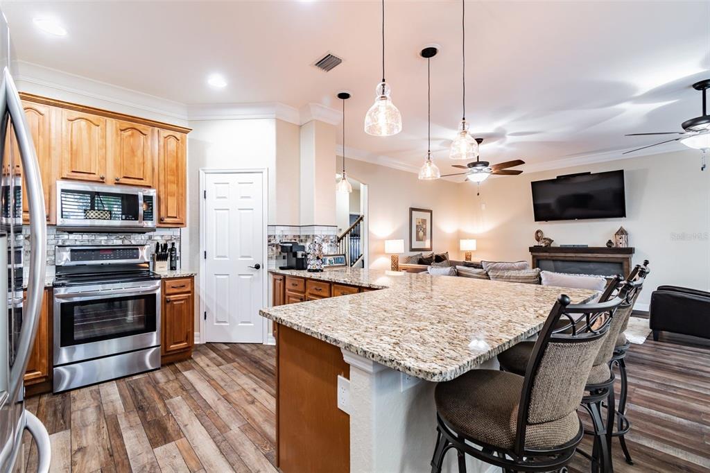 A kitchen with wood cabinets, granite countertops, and an island opens into a living room — 539 TREVISO DRIVE, APOLLO BEACH, FL