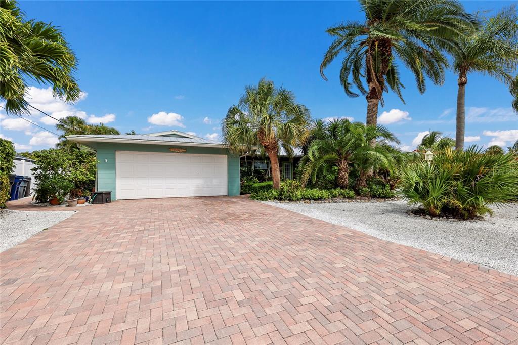 A teal house with a white garage door sits behind a brick paver driveway — 5007 BIMINI DRIVE, BRADENTON, FL