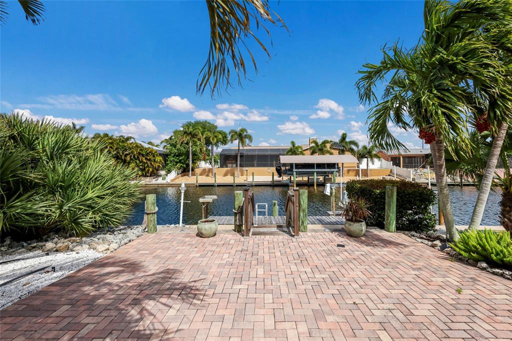 A brick patio overlooks a canal with a boat lift and a wooden dock — 5007 BIMINI DRIVE, BRADENTON, FL