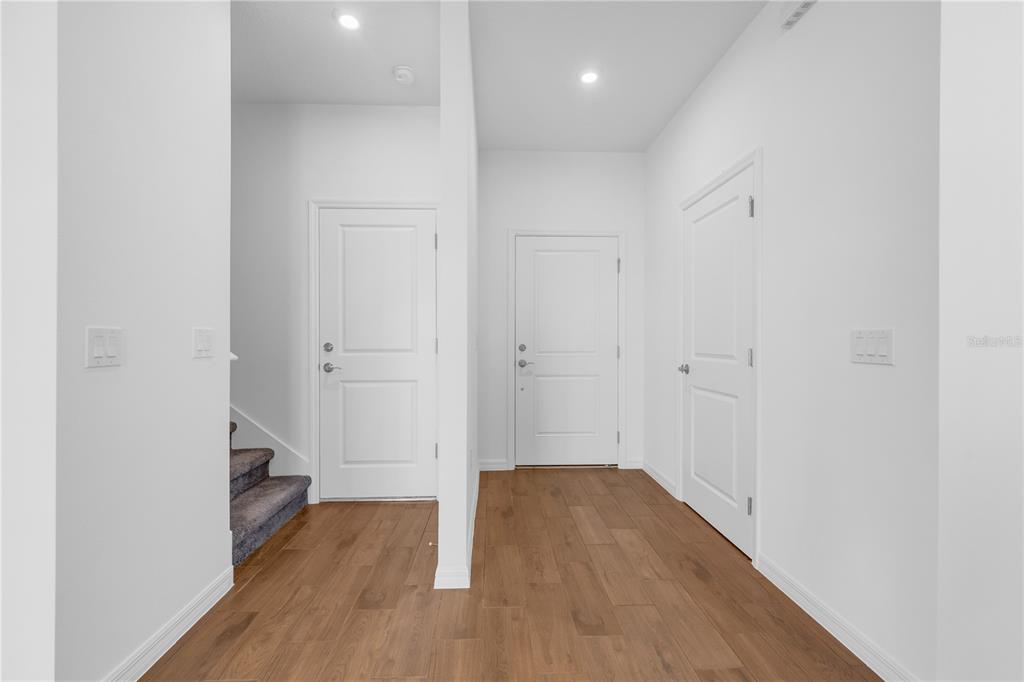 An interior hallway features white walls, wood-look flooring, two closed doors, and a carpeted staircase — 4450 RIVER BEACON BOULEVARD, DAVENPORT, FL