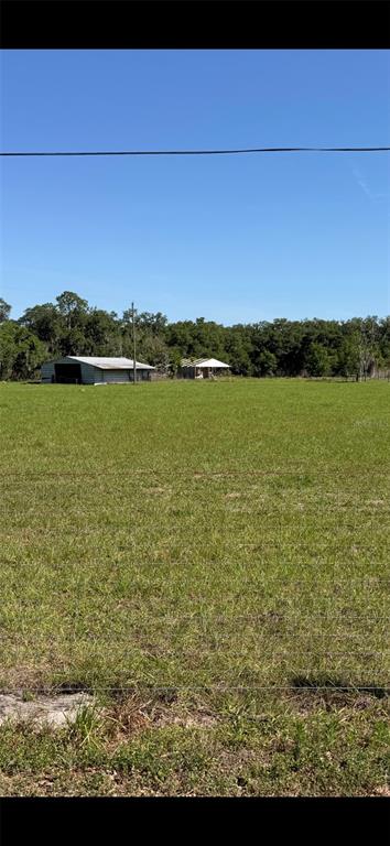 A large, open grassy field features a metal barn and a small house in the distance — SYDNEY ROAD, DOVER, FL