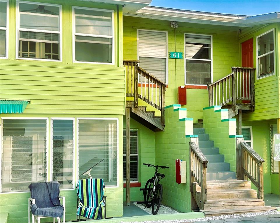 A lime green two-story apartment building features exterior wooden staircases and a bicycle parked underneath — 61 81ST AVENUE UNIT 3, TREASURE ISLAND, FL
