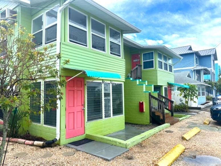 A two-story lime green building features a bright pink door and a blue awning — 61 81ST AVENUE UNIT 3, TREASURE ISLAND, FL