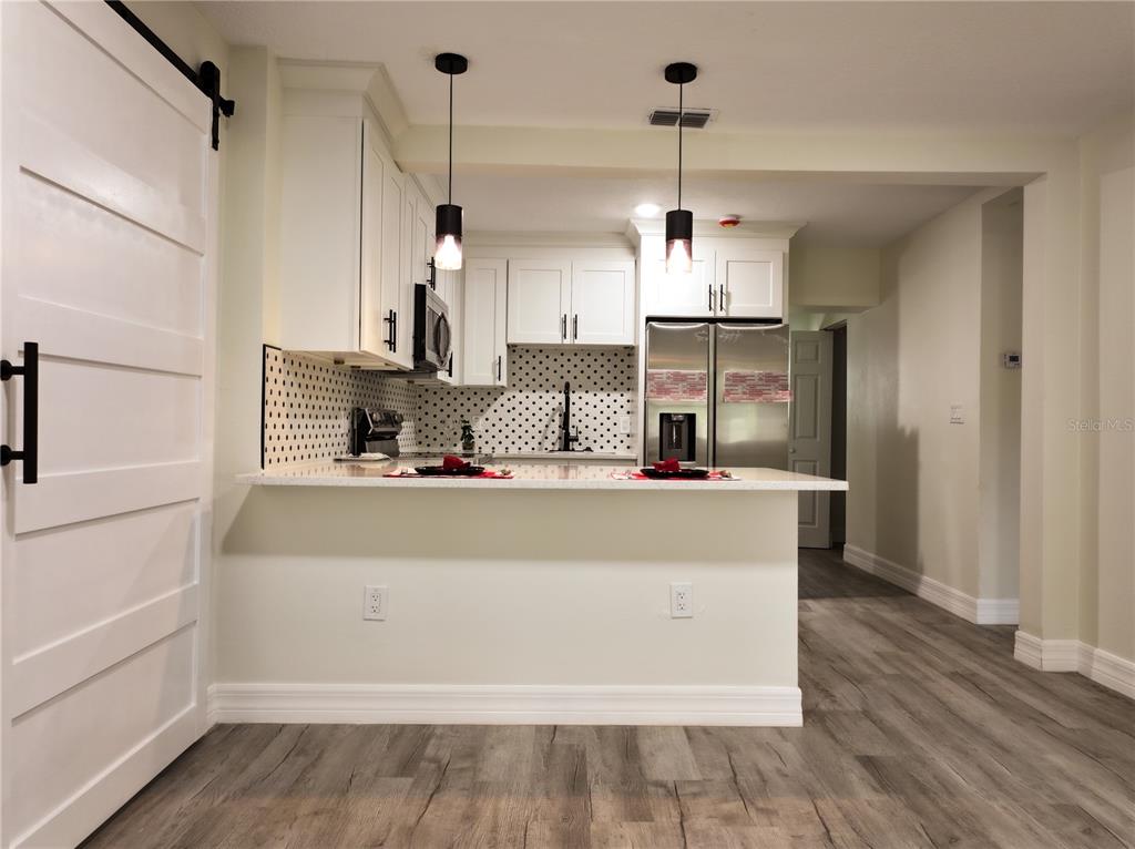 A kitchen with white cabinets, a polka-dot backsplash, stainless steel appliances, and wood-look flooring — 919 W HIAWATHA STREET, TAMPA, FL