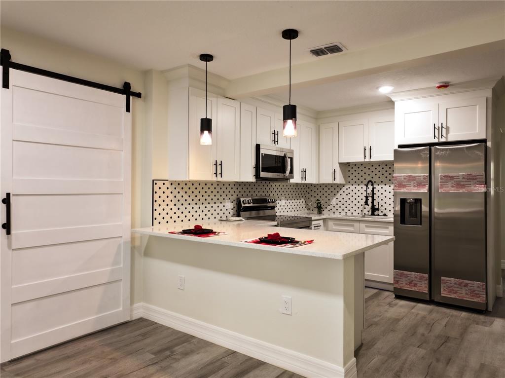 A modern kitchen features white cabinets, a polka-dot backsplash, stainless steel appliances, and a breakfast bar — 919 W HIAWATHA STREET, TAMPA, FL