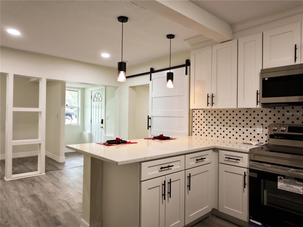 A kitchen with white cabinets, a polka-dot backsplash, and a quartz-topped island with pendant lighting — 919 W HIAWATHA STREET, TAMPA, FL