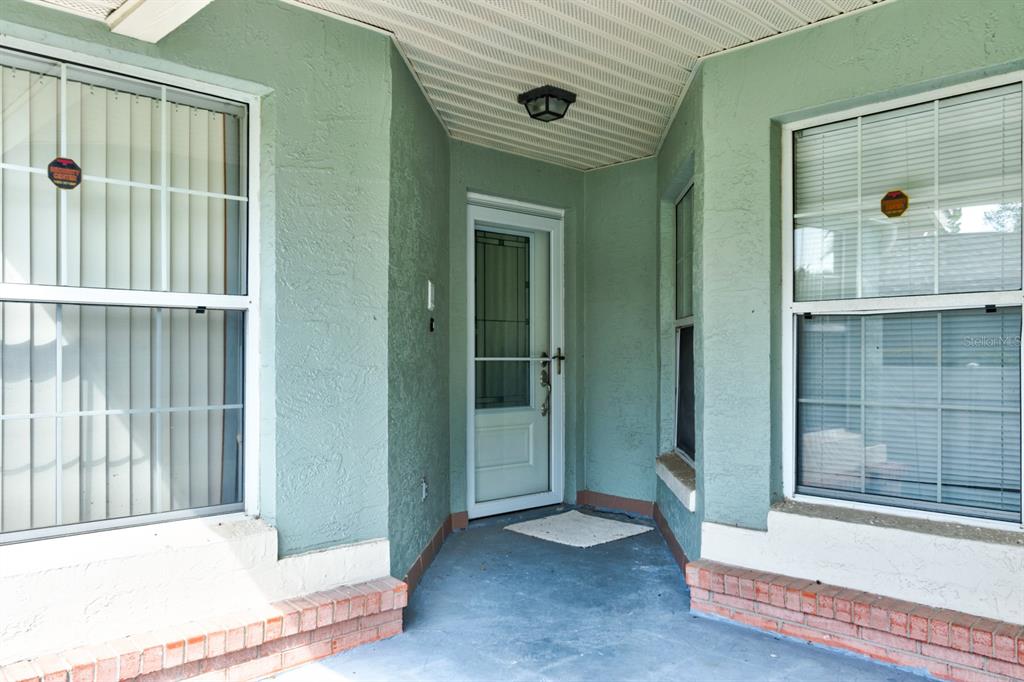 A covered entryway with a light green stucco exterior, a white storm door, and two windows — 317 GLENBRIAR CIRCLE, DAYTONA BEACH, FL
