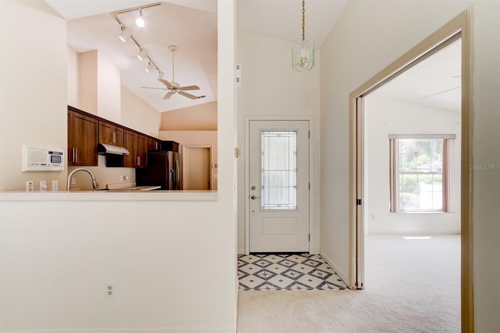 An entryway with patterned tile flooring leads to a kitchen and an adjacent carpeted room — 317 GLENBRIAR CIRCLE, DAYTONA BEACH, FL