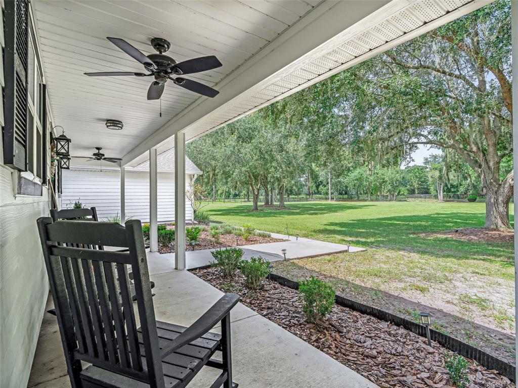 A covered porch with a rocking chair overlooks a grassy yard with large oak trees — 1539 SE 34TH WAY, SUMTERVILLE, FL