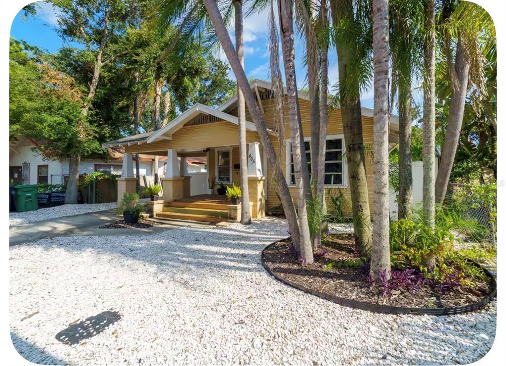 A yellow bungalow with a front porch and palm trees sits behind a gravel yard — 405 E ADALEE STREET, TAMPA, FL