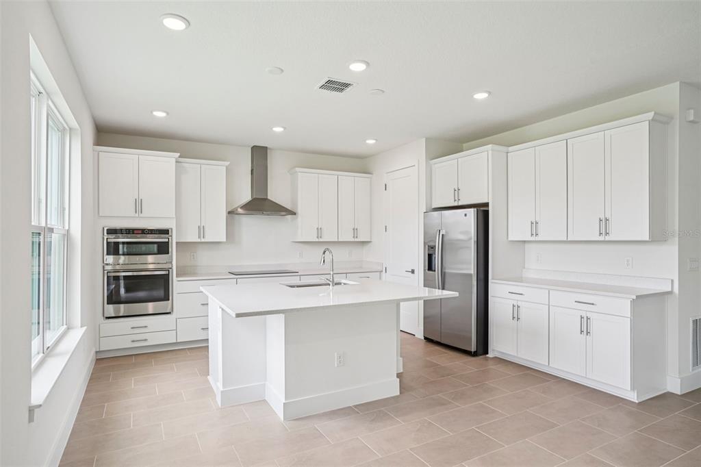 A modern kitchen features white cabinets, stainless steel appliances, a center island, and tile flooring — 30333 EMERALD FOREST DRIVE, MOUNT DORA, FL