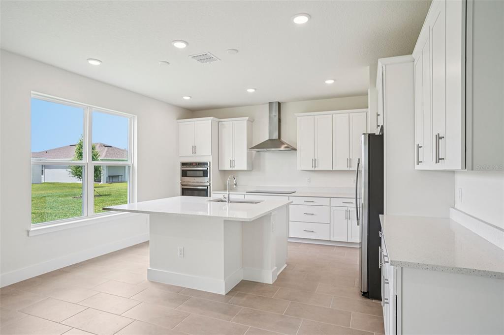 A modern white kitchen features a central island, stainless steel appliances, and tile flooring — 30333 EMERALD FOREST DRIVE, MOUNT DORA, FL