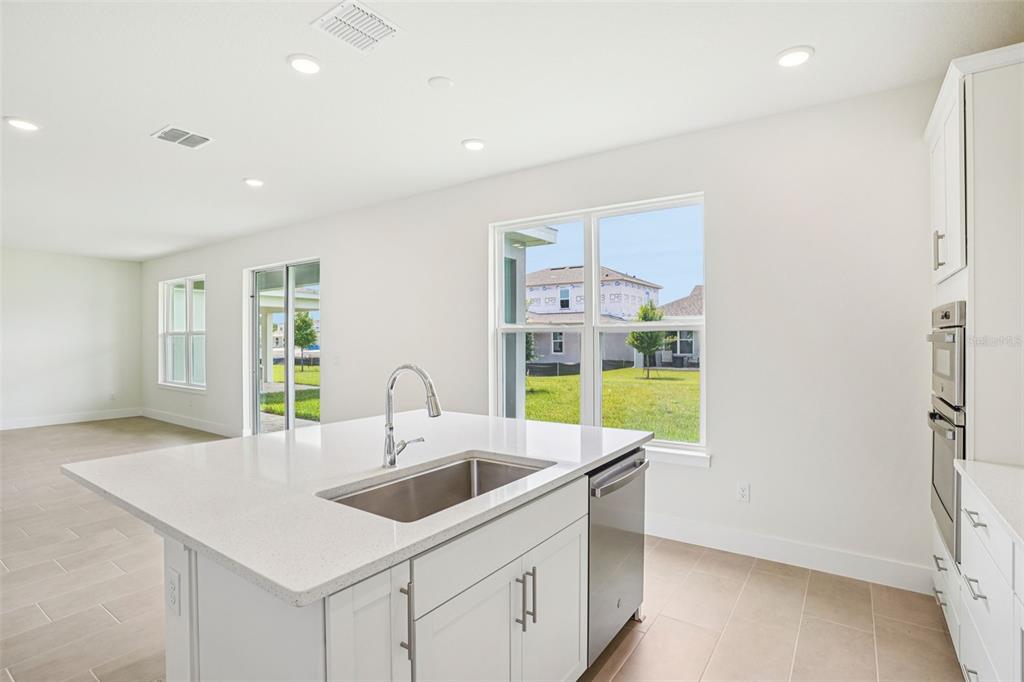 A modern kitchen features a white quartz island with a sink and stainless steel appliances — 30333 EMERALD FOREST DRIVE, MOUNT DORA, FL