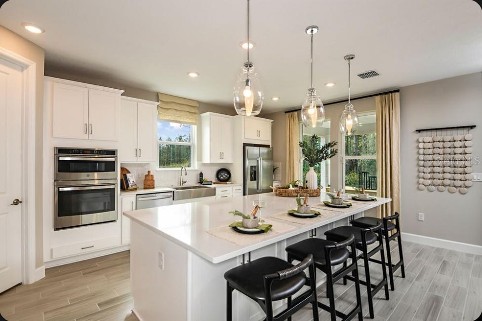 A modern kitchen features white cabinetry, a large quartz island, and three black bar stools — 50 GRECO DRIVE, PALM COAST, FL