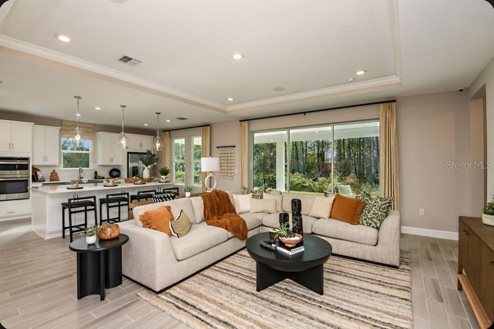 A modern open-concept living room features a large sectional sofa, kitchen island, and sliding glass doors — 50 GRECO DRIVE, PALM COAST, FL