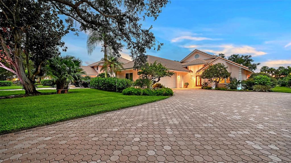 A large house with a paved driveway, manicured lawn, and mature trees at dusk — 5476 GOLF POINTE DRIVE, SARASOTA, FL