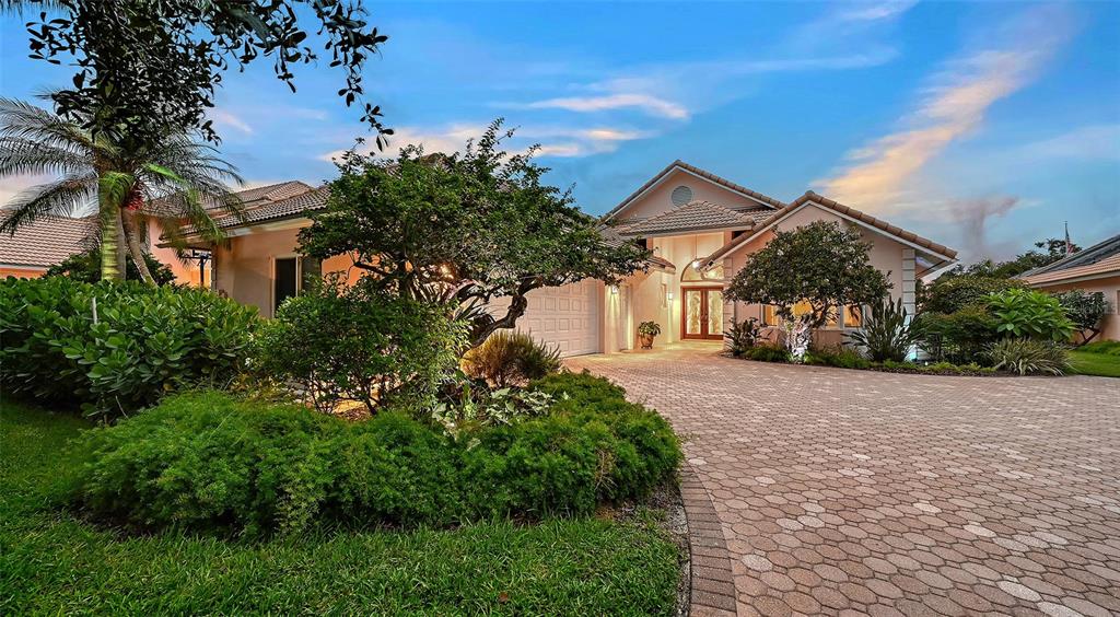 A single-story house with a paved driveway, lush landscaping, and a tiled roof at dusk — 5476 GOLF POINTE DRIVE, SARASOTA, FL