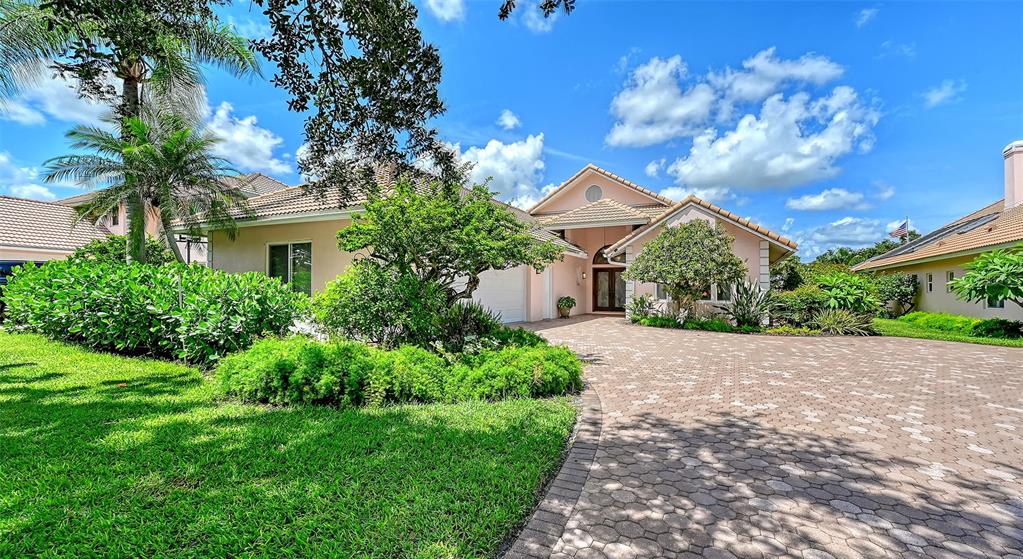 A pale pink house with a paved driveway and lush landscaping under a blue sky — 5476 GOLF POINTE DRIVE, SARASOTA, FL