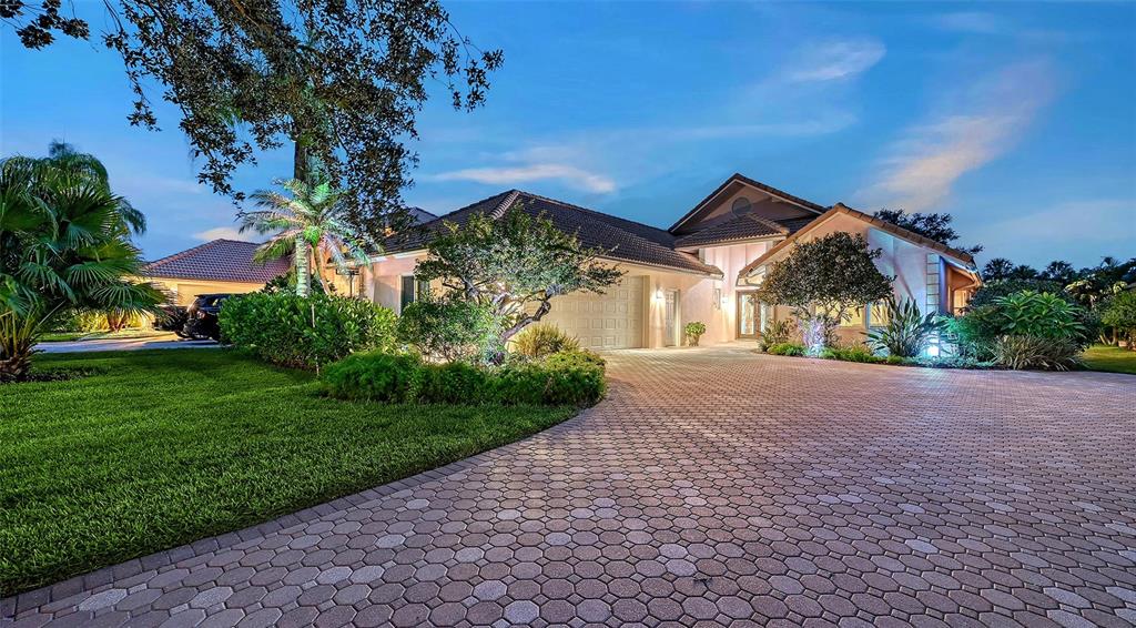 A large single-story house with a paved driveway and landscaped yard at dusk — 5476 GOLF POINTE DRIVE, SARASOTA, FL