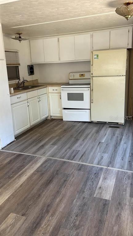 A kitchen features white cabinets, a white stove, a refrigerator, and wood-look laminate flooring — 212 SUNSET DRIVE, LAKE ALFRED, FL