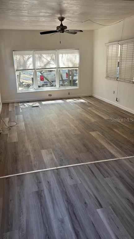 An empty room features wood-look flooring, a ceiling fan, and large windows with blinds — 212 SUNSET DRIVE, LAKE ALFRED, FL