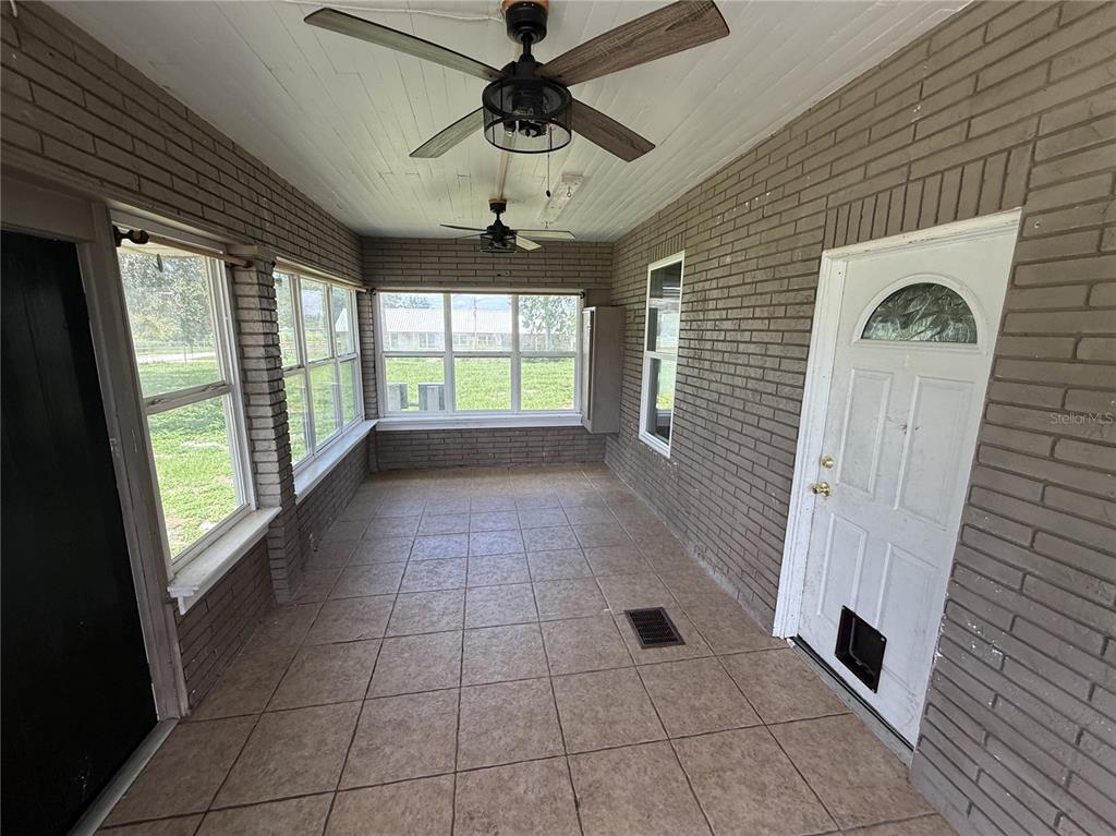 A sunroom features brick walls, tiled flooring, two ceiling fans, and a white exterior door — 1115 KELLER ROAD, FORT MEADE, FL