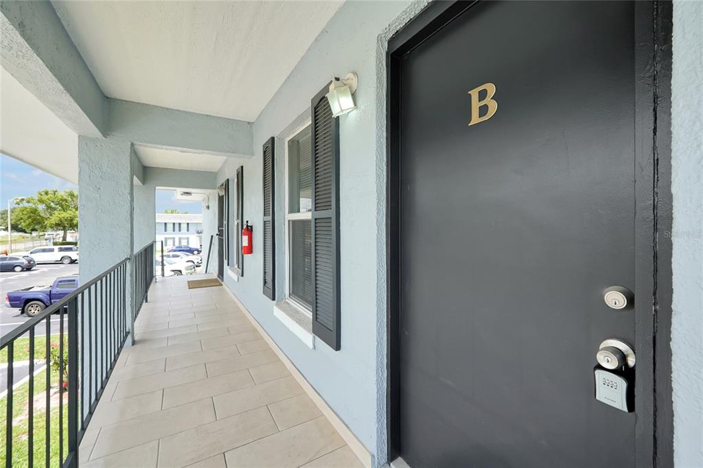 A covered outdoor walkway with light-colored tile flooring leads to a dark door labeled B — 915 W OAK RIDGE ROAD UNIT B, ORLANDO, FL