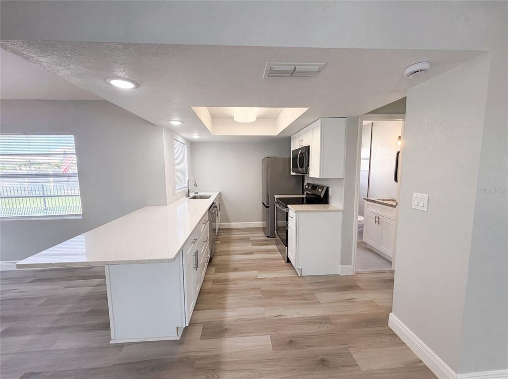A modern kitchen features white cabinets, quartz countertops, stainless steel appliances, and wood-look flooring — 7428 MAKO DRIVE, HUDSON, FL
