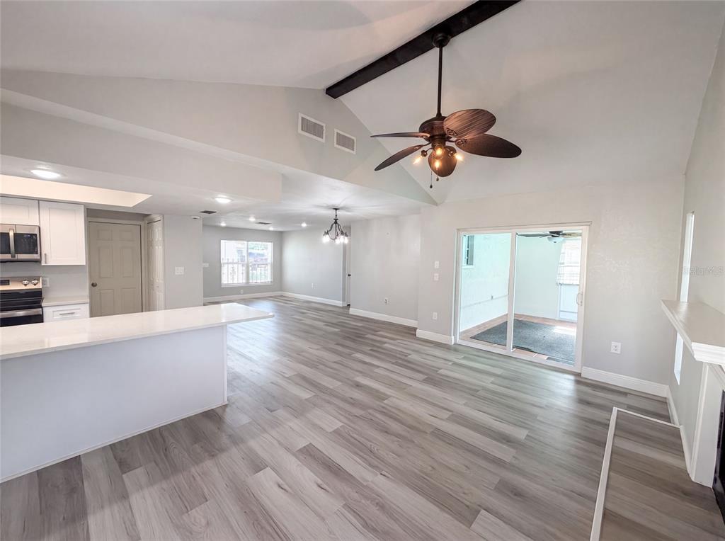 An open-concept living area features vaulted ceilings, a ceiling fan, and light wood-look flooring — 7428 MAKO DRIVE, HUDSON, FL