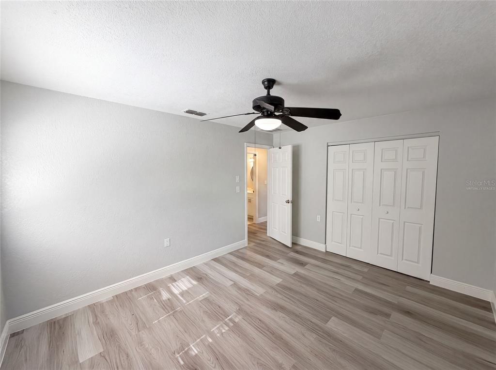 A bedroom with light gray walls, wood-look flooring, a ceiling fan, and white closet doors — 7428 MAKO DRIVE, HUDSON, FL