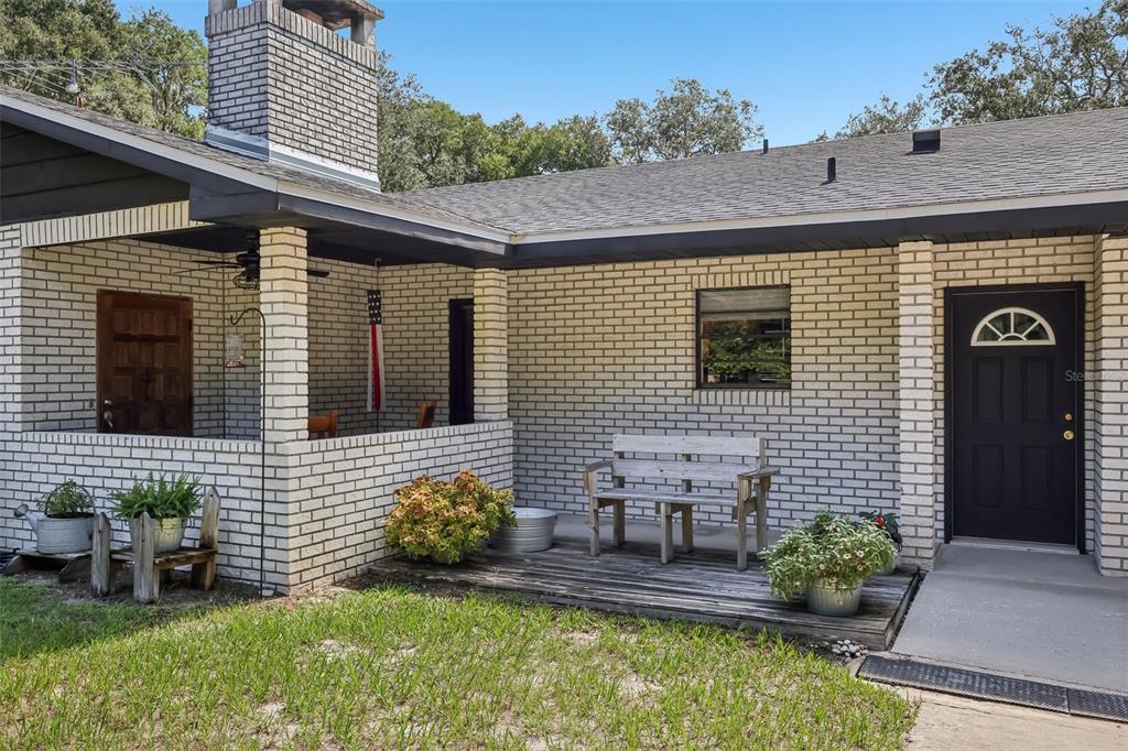 A brick house exterior features a covered porch, a wooden bench, and a black front door — 209 JASPER STREET, BUSHNELL, FL