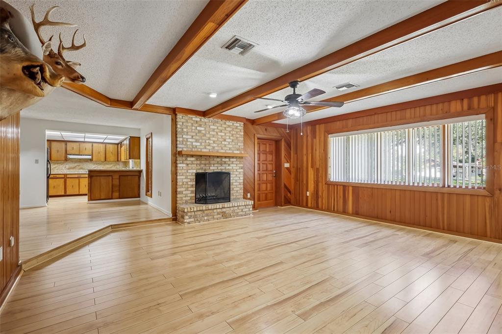 A living room with wood-paneled walls, a brick fireplace, exposed ceiling beams, and hardwood floors — 209 JASPER STREET, BUSHNELL, FL